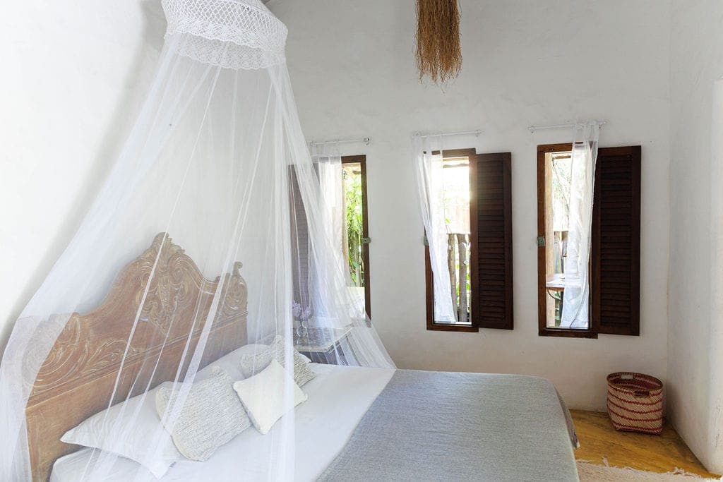 Quarto da Vila Bahia com dossel branco e janelas de madeira